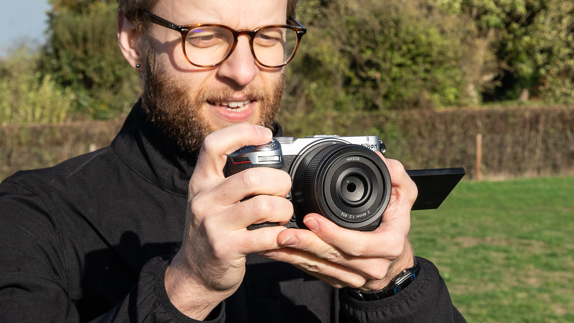Mike Harris wearing a black jacket holding the Nikon Z5IIC on a green background
