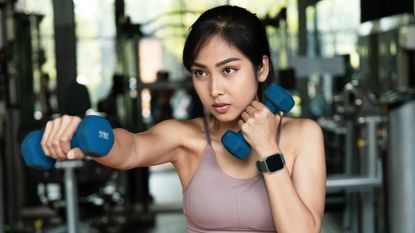 Woman punches the air with a light pair of dumbbells in her hands