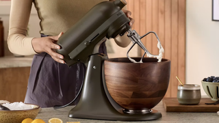 Woman using KitchenAid Artisan stand mixer in Evergreen with wooden bowl