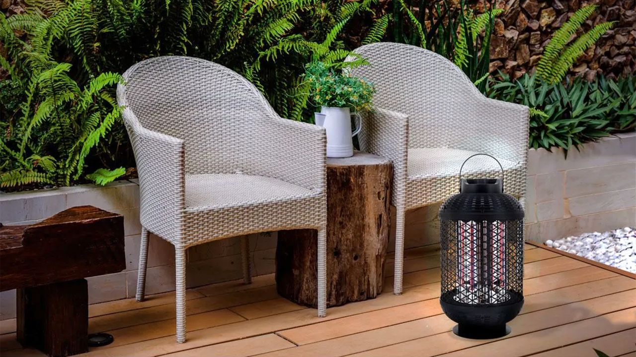 A small black lantern-shaped electric patio heater on the floor in front of two grey rattan chairs