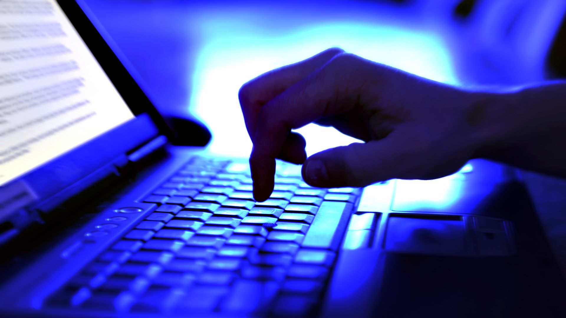 A person typing on a laptop, bathed in blue light