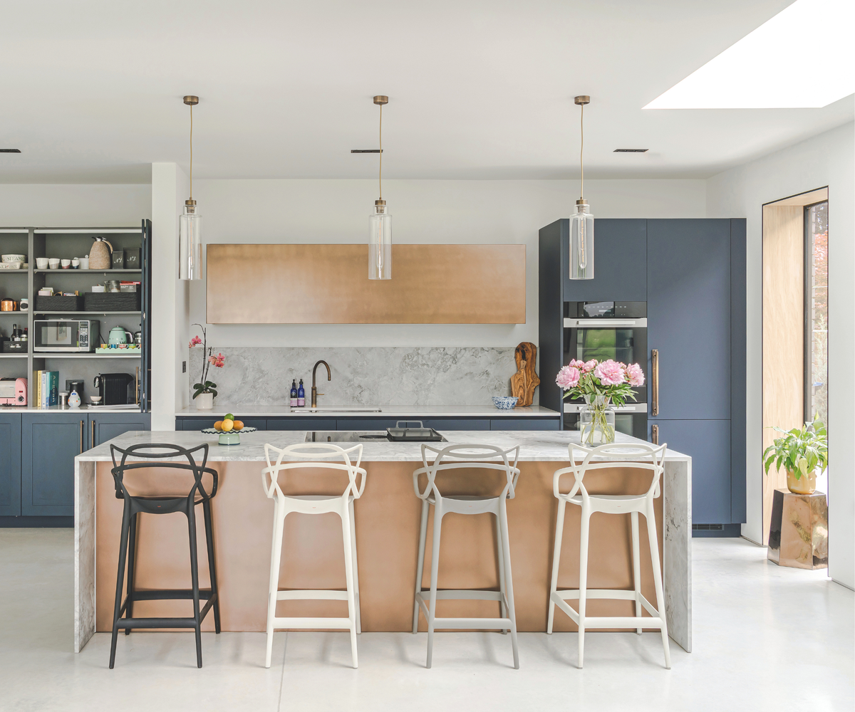 Kitchen with island, marble splashback and worktop, and a mix of navy and gold cabinets
