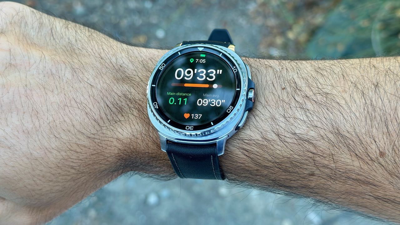 The Samsung Galaxy Watch 8 Classic on a wrist showing a Running Coach workout screen with current pace, distance, average pace, heart rate, and time.