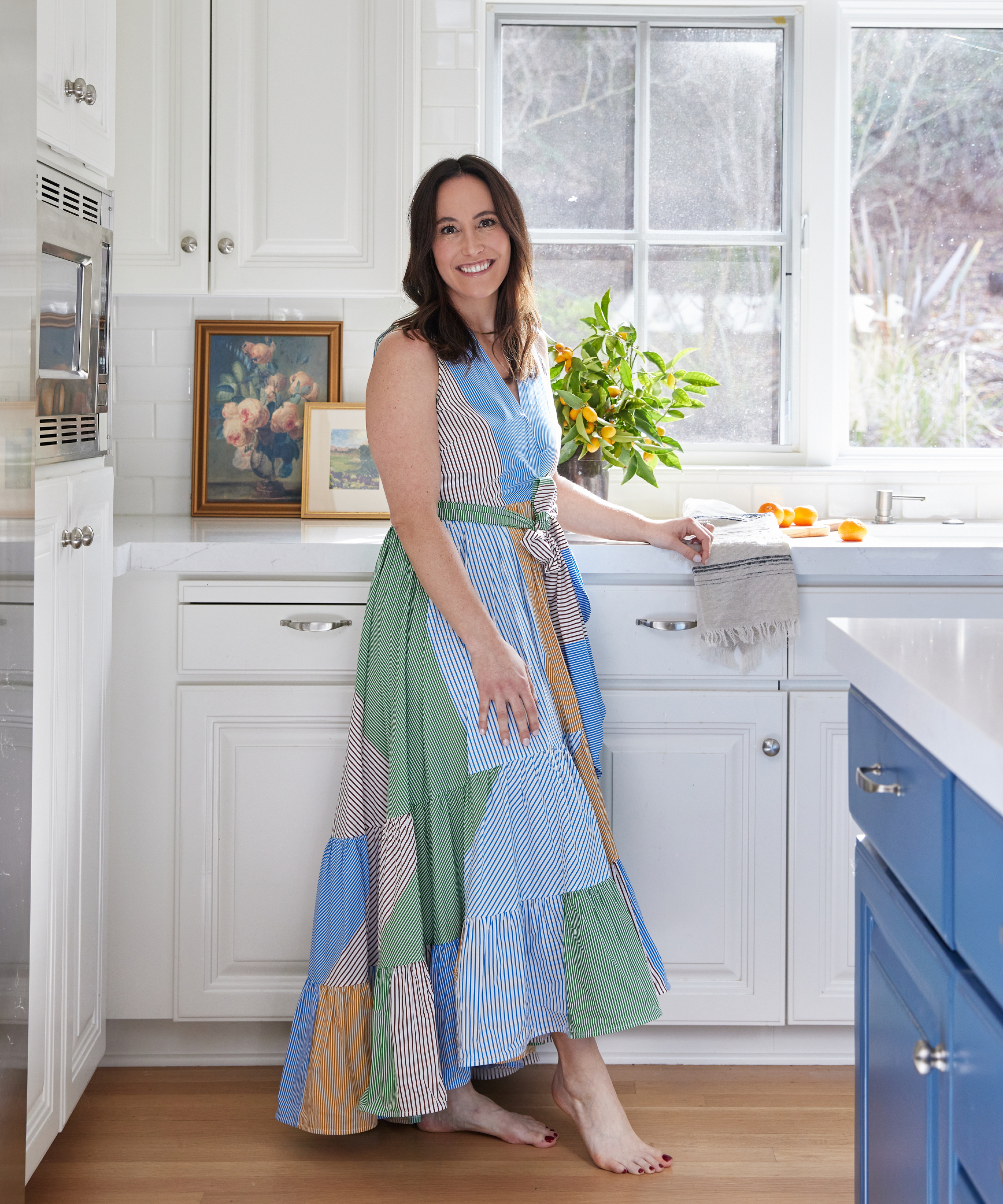 expert headshot of Emily Flaxman, Flax Interiors, a dark haired woman wearing a patchwork style dress in a white kitchen 