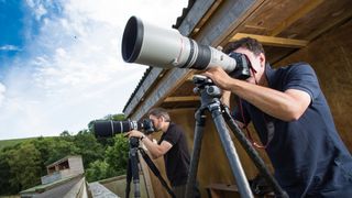 Two wildlife photographers in hide with long telephoto lenses