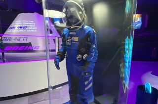 Adam Savage's replica of ILC Dover's Ascent and Entry Suit (AES) for Boeing's CST-100 Starliner crew spacecraft is on display alongside a Starliner mockup and simulator in Kennedy Space Center Visitor Complex's new attraction, "Gateway: The Deep Space Complex."