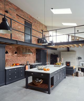 Industrial grey kitchen with grey cabinets and an exposed brick wall.