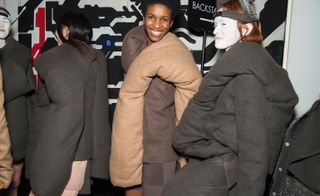 Models are seen wearing dark grey and beige cloud coats, with pillowing lapels. One model wears white facepaint.