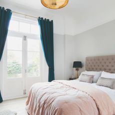 A bright bedroom with dark teal velvet eyelet curtains and a pink quilted headboard on the double bed