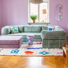 A corner version of the Teddy sofa and coordinating ottoman by OMHU in Sage and Purple in a living room with lilac walls and patterned soft furnishings