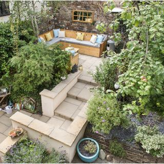 Makeover of a split level garden. L-shaped sitting area with cushions on wooden benches