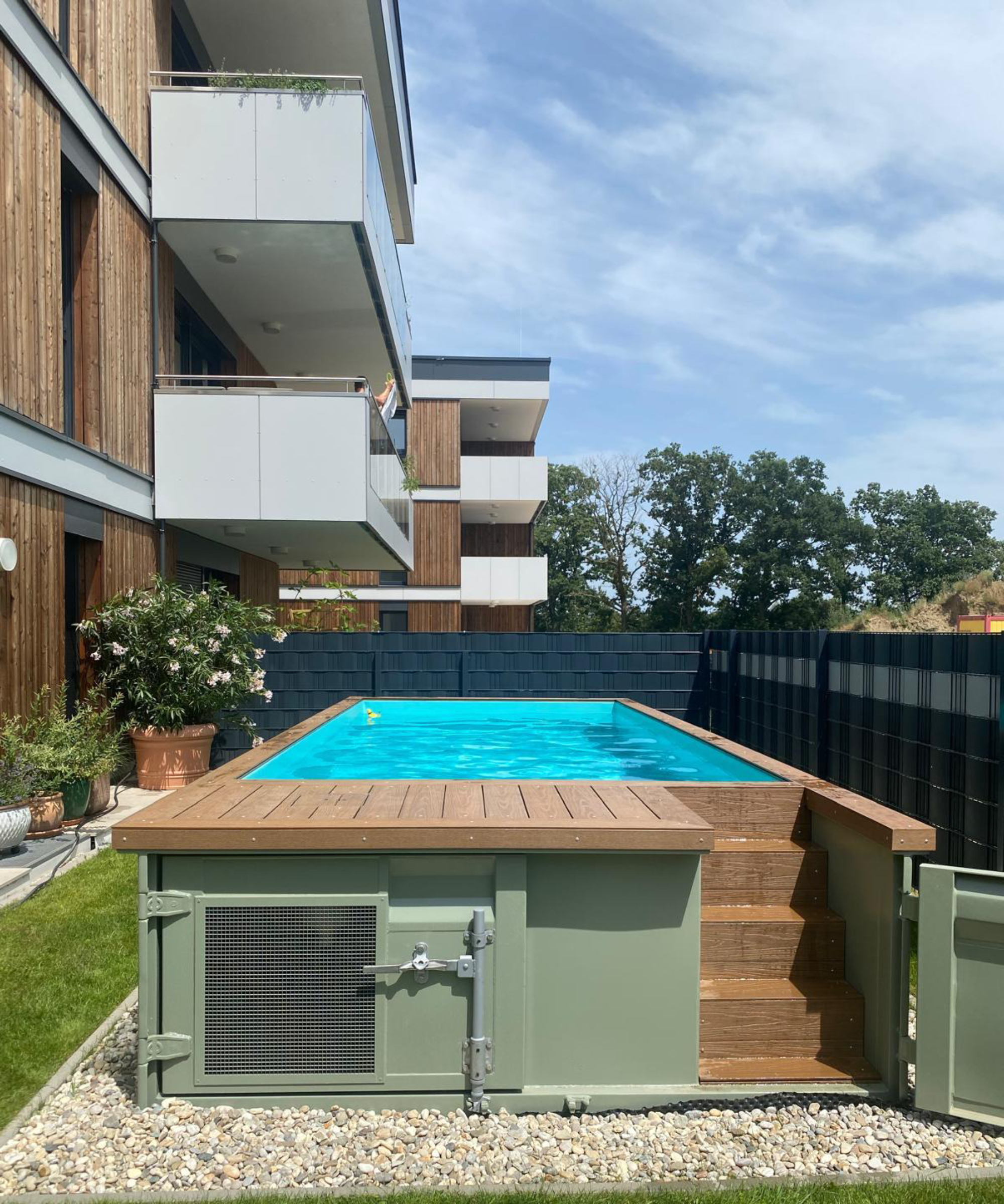 above ground shipping container swimming pool in garden of an apartment block on compacted gravel base