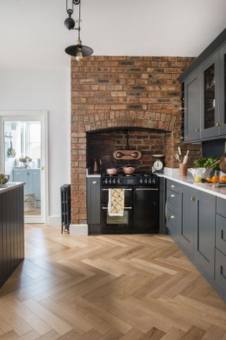 A grey kitchen with exposed brick wall and Herringbone style wooden flooring