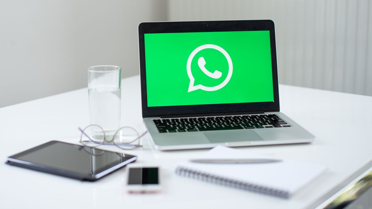 A laptop on a cluttered desk with WhatsApp logo displayed on screen