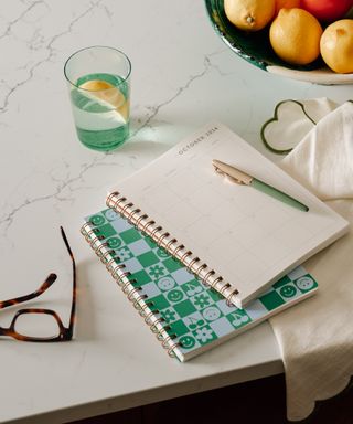 marble countertop with notebooks and pen, fruit bowl, glass of water, glasses, napkin