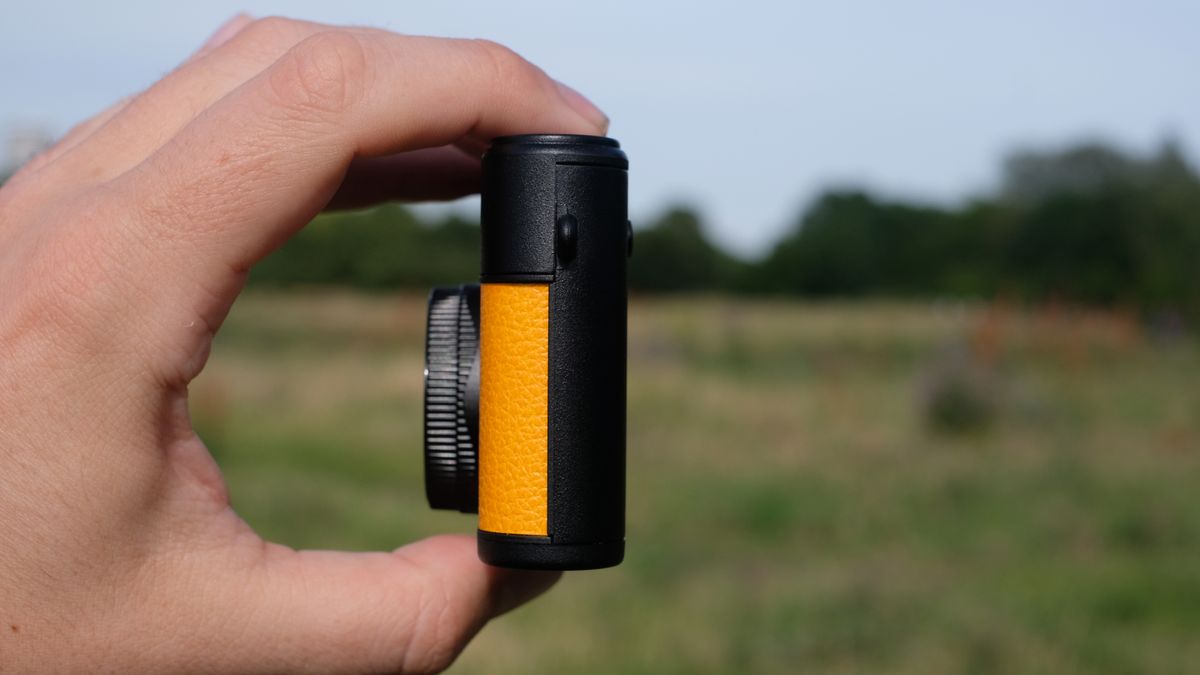 Photograph of man's hand holding Camp Snap 2 digital camera, in yellow colorway, side view facing left