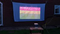 A photo of football being projected onto a white sheet against the wall of a house in a garden