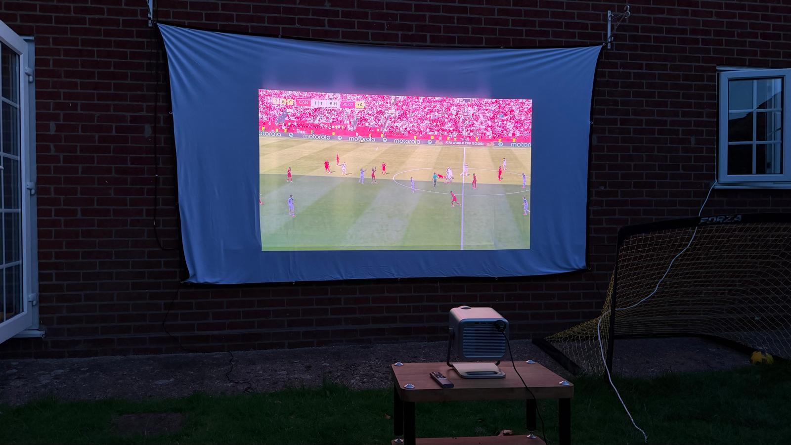 A photo of football being projected onto a white sheet against the wall of a house in a garden