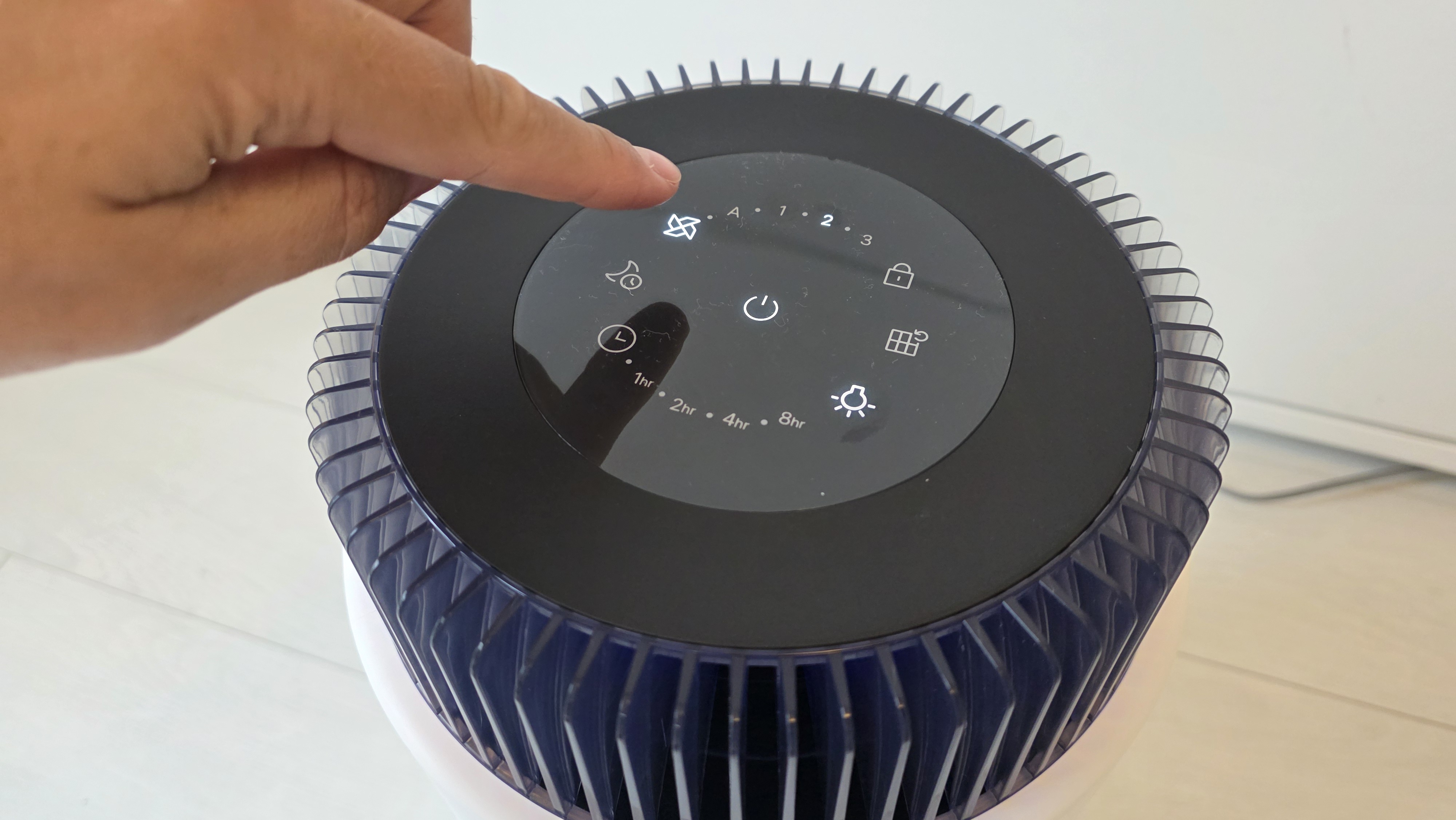 A man's finger hovers over the Coway Airmega 100's fan button.