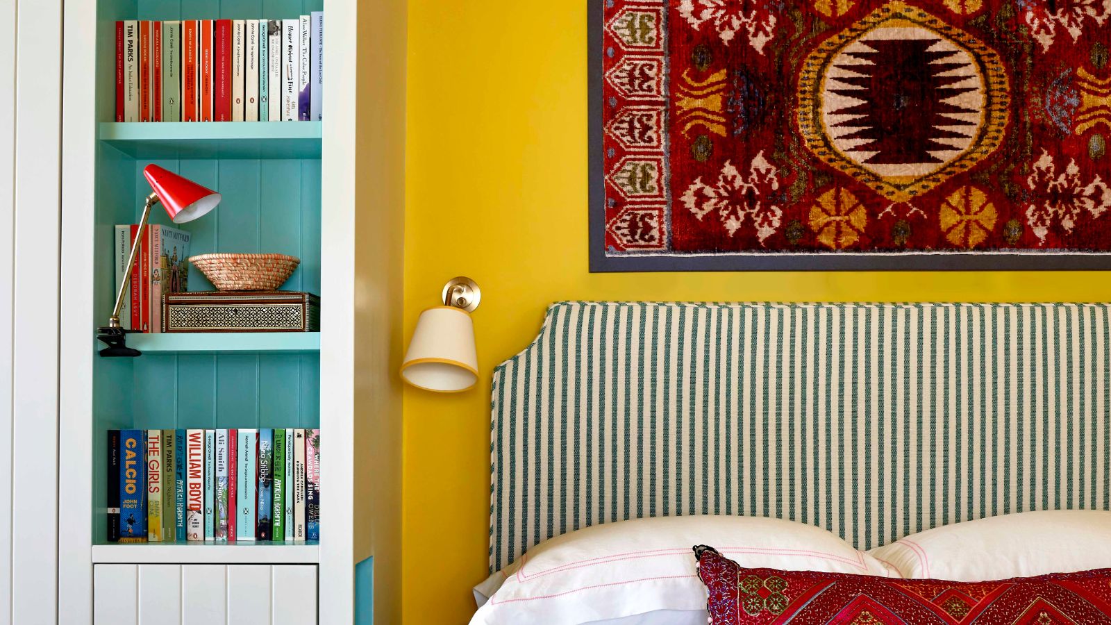 Yellow bedroom with striped headboard and light blue built in narrow storage unit filled with books