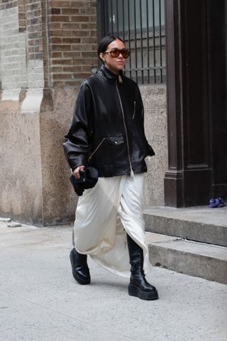 A woman at New York Fashion Week in a leather jacket and white skirt