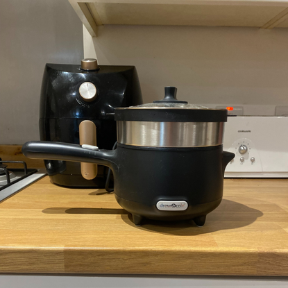 The CleverPot on a wooden kitchen countertop in front of a small black air fryer and white toaster.