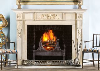 traditional antique carved stone fireplace with fire burning in the grate westland london