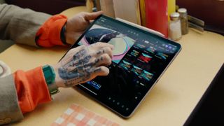 A photo of someone with tattooed hands using Final Cut Pro on an iPad to edit a video at a table