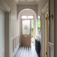 A narrrow hallway painted cream with dado rail wall panelling and tiled black and white chequered floor