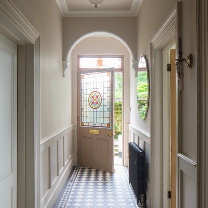 A narrrow hallway painted cream with dado rail wall panelling and tiled black and white chequered floor