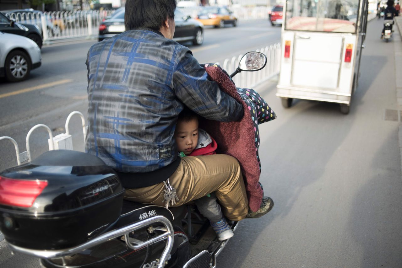 A man transports his son on a scooter along a road in Beijing