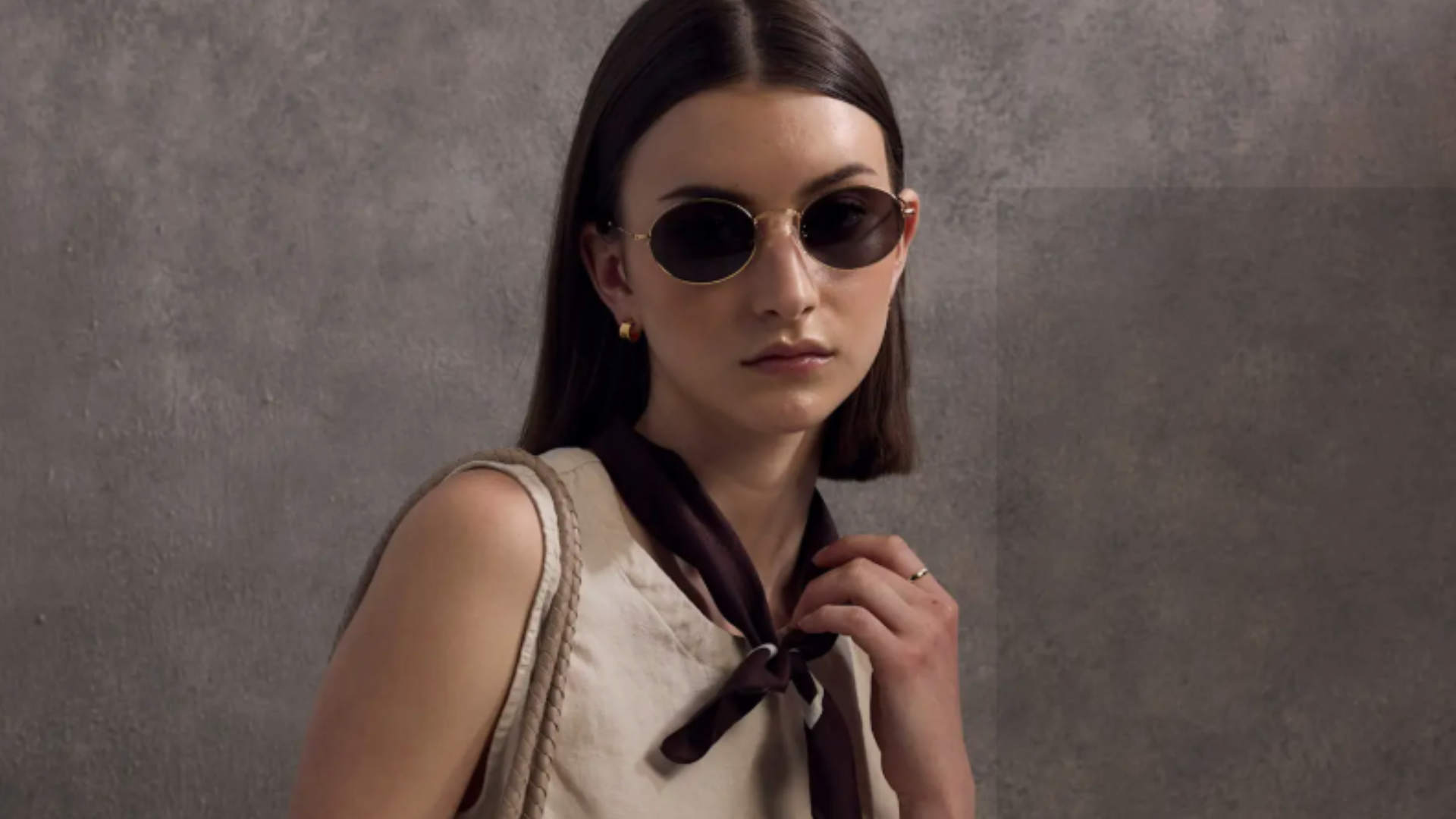 woman wearing oval sunglasses and a tan top.