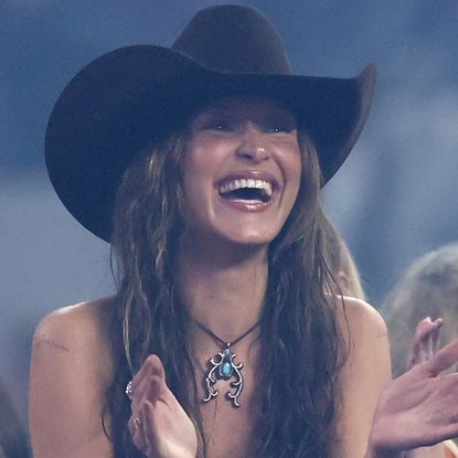 Bella Hadid wears a cowboy hat and applauds and puts her hands on her boyfriend Adan Banuelos' face while watching The American Performance Horseman by Teton Ridge at Globe Life Field