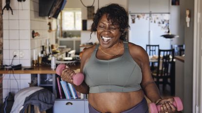 Joyful middle aged woman working out at home with dumbbells