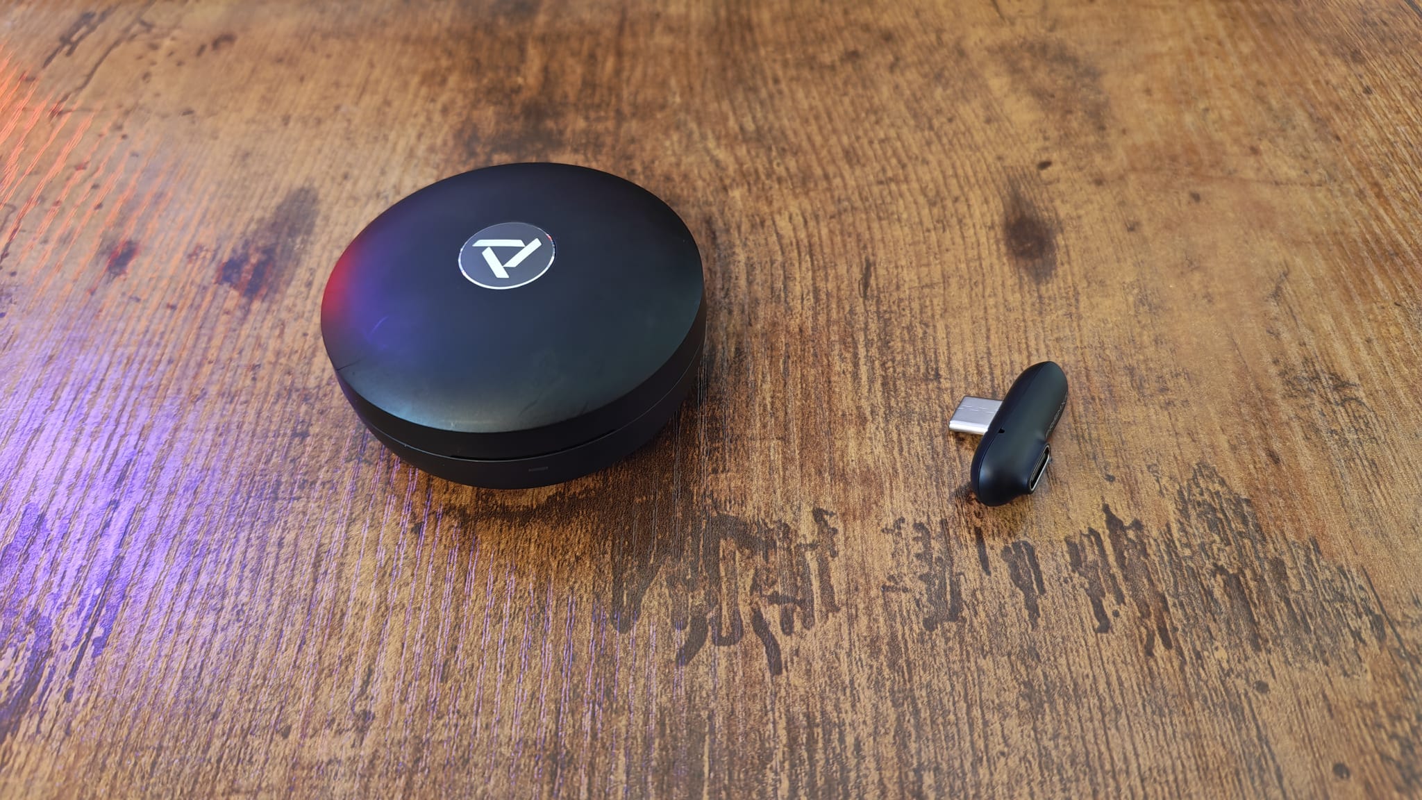 The circular PrismXR Vega T1 earbuds case next to its dongle