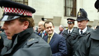 LONDON, UNITED KINGDOM: Paul Burrell (C) is escorted from the Central Criminal Court after the case against him of stealing from the estate of Diana, Princess of Wales, the Prince of Wales and Prince William, in London 01 November 2002. The trial against the former butler came to a premature end because of the sudden involvement of the Queen and the Prince of Wales. It emerged that Burrell told The Queen he had been keeping items belonging to Diana for safe keeping. AFP PHOTO Adrian DENNIS (Photo credit should read ADRIAN DENNIS/AFP via Getty Images)