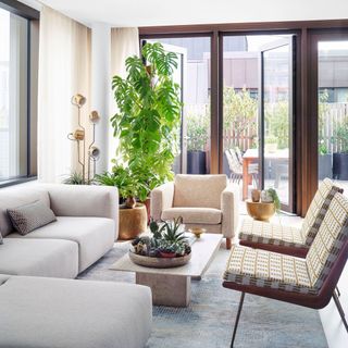 Living with floor to ceiling windows, neutral sofa, patterned armchairs and houseplant