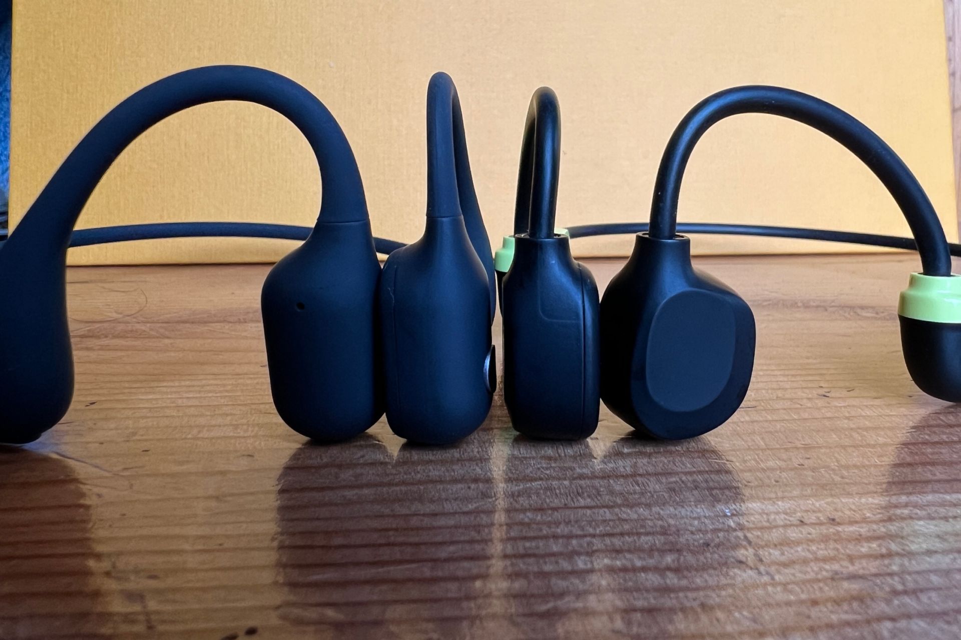 Haylou PurFree Lite Vs BC01 vibrating units side by side on a wooden surface with a yellow background