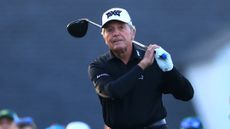 Gary Player wearing a black long sleeve polo and white PXG cap while holding his finish on a drive