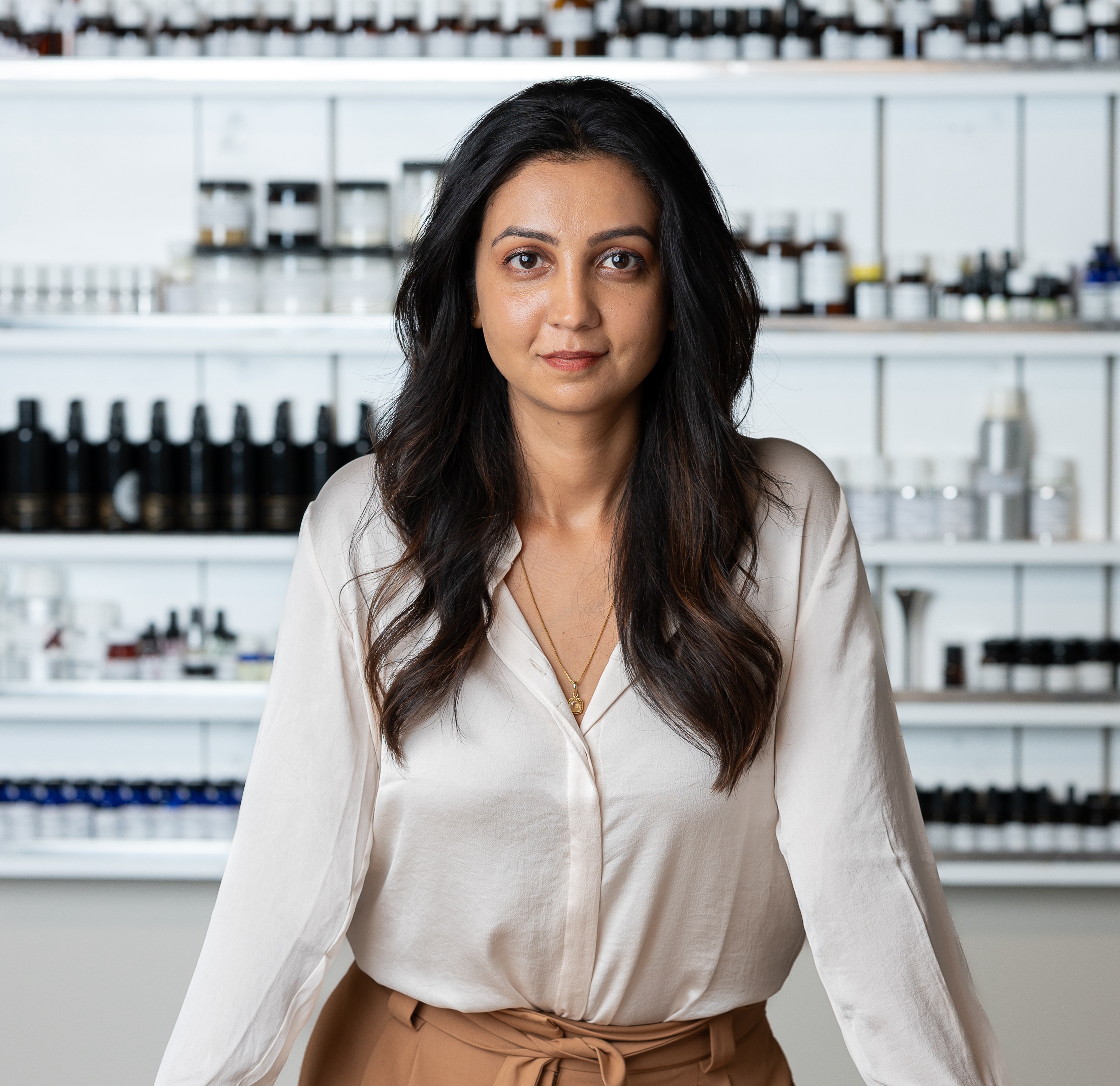 a woman with dark brown hair in a white shirt in front of a wall of products