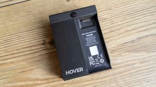 The HoverAir's black charging battery block sits on a wooden table.
