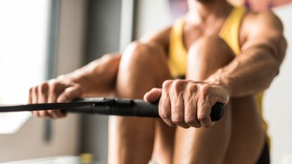 A person's hand grips the handles of a rowing machine mid exercise