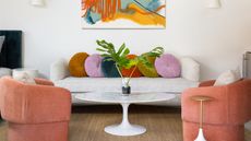 living room with jute rug, two coral armchairs, a white sofa with colorful pillows and a white marble coffee table with a vase with two branches