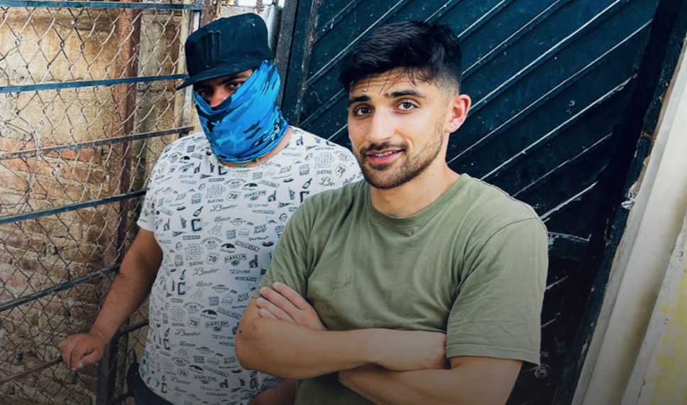 Documentary-maker Ben Zand poses next to an electric fence with a sinister-looking member of the Sinaloa Cartel in a face mask.