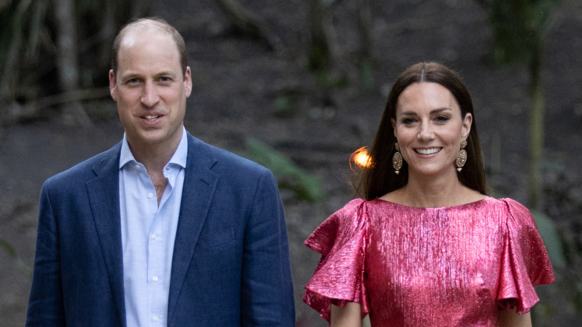 Prince William wears a navy suit with a light blue shirt and Kate Middleton wears a metallic pink dress