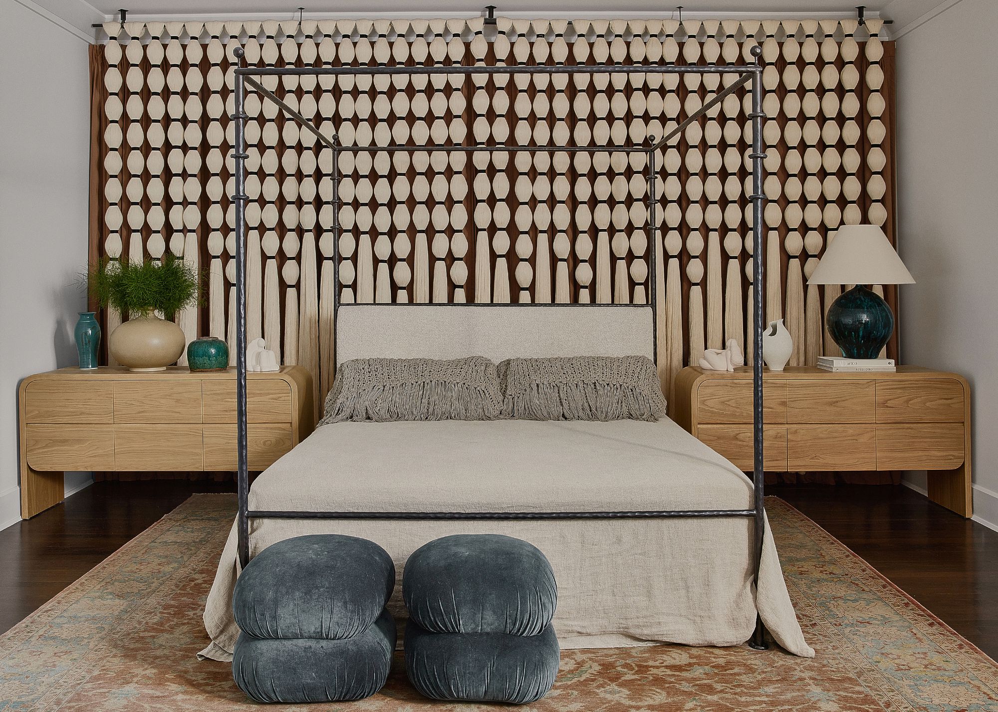 A bedroom with long tassels behind the bed, two side tables next to the bed and a vintage carpet