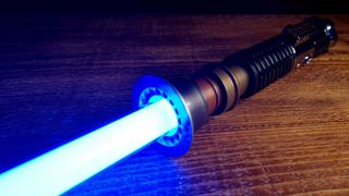 Star Wars The Black Series Obi-Wan Kenobi Force FX Elite Lightsaber, with blade activated, on a wooden table