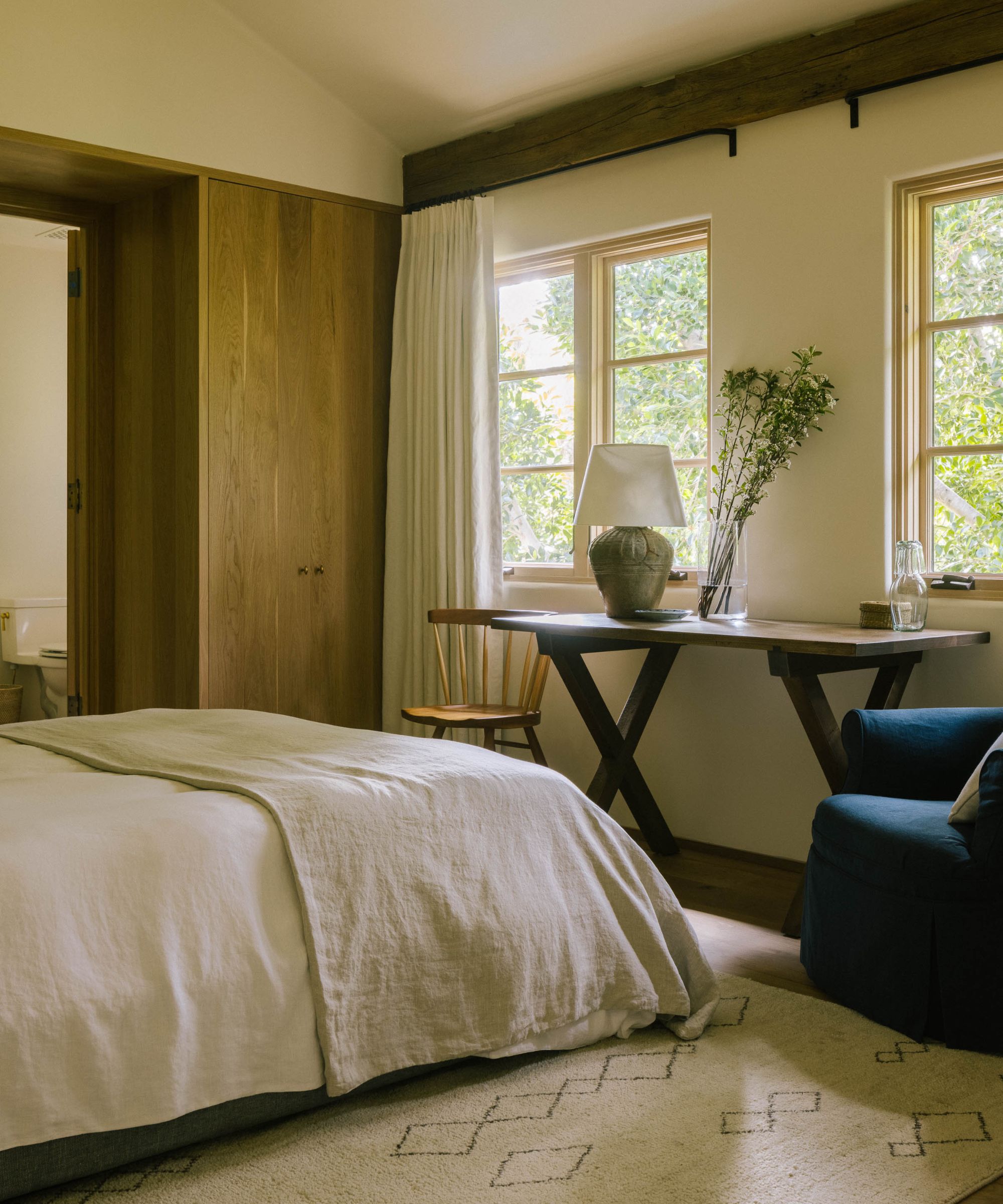 a rustic meets European bedroom with ceiling beams, neutral bed, natural linens, and oak closets