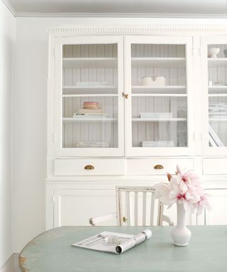 white kitchen dresser with light blue-green table with vase of pale pink flowers