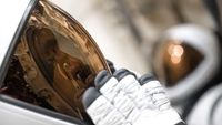 A closeup of a white-shelled astronaut helmet from the left, extending to the middle of the image. A copper-shaded visor stretches across the dimmed interior face. A black-tipped white glove tests on the visor.